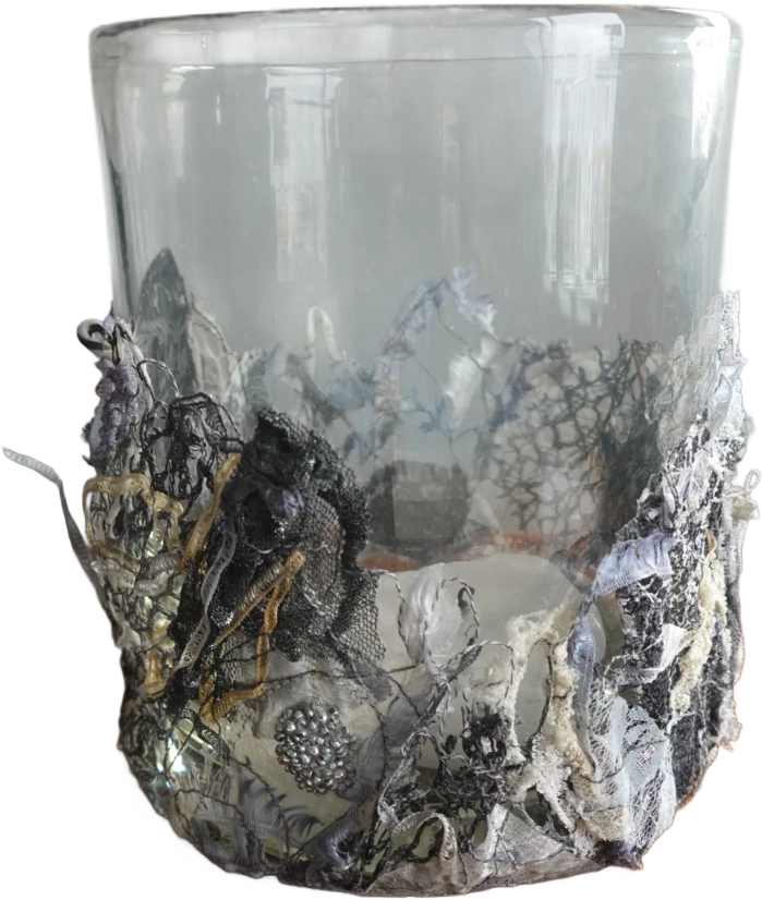Gegnsætt glas með hvítu, gráu og svörtu blúndulíku skrauti á neðri hlutanum.